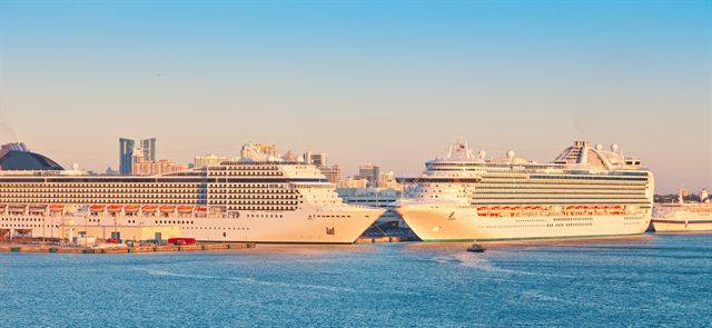 Two large cruise ships berthed at a cruise terminal in warm evening light