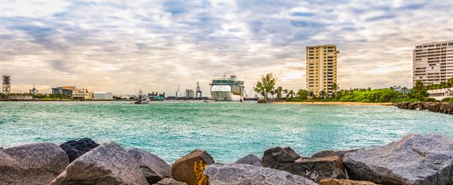 Cruise ship in the harbour inlet seen past rock jetty boulders and beachfront high-rises