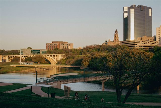 Fort Worth skyline and Tarrant County Courthouse above the Trinity River, arched bridge and park at golden hour