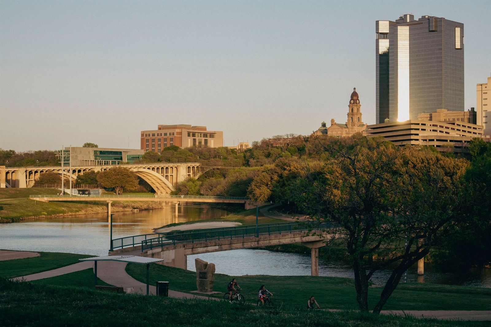 Fort Worth skyline and Tarrant County Courthouse above the Trinity River, arched bridge and park at golden hour