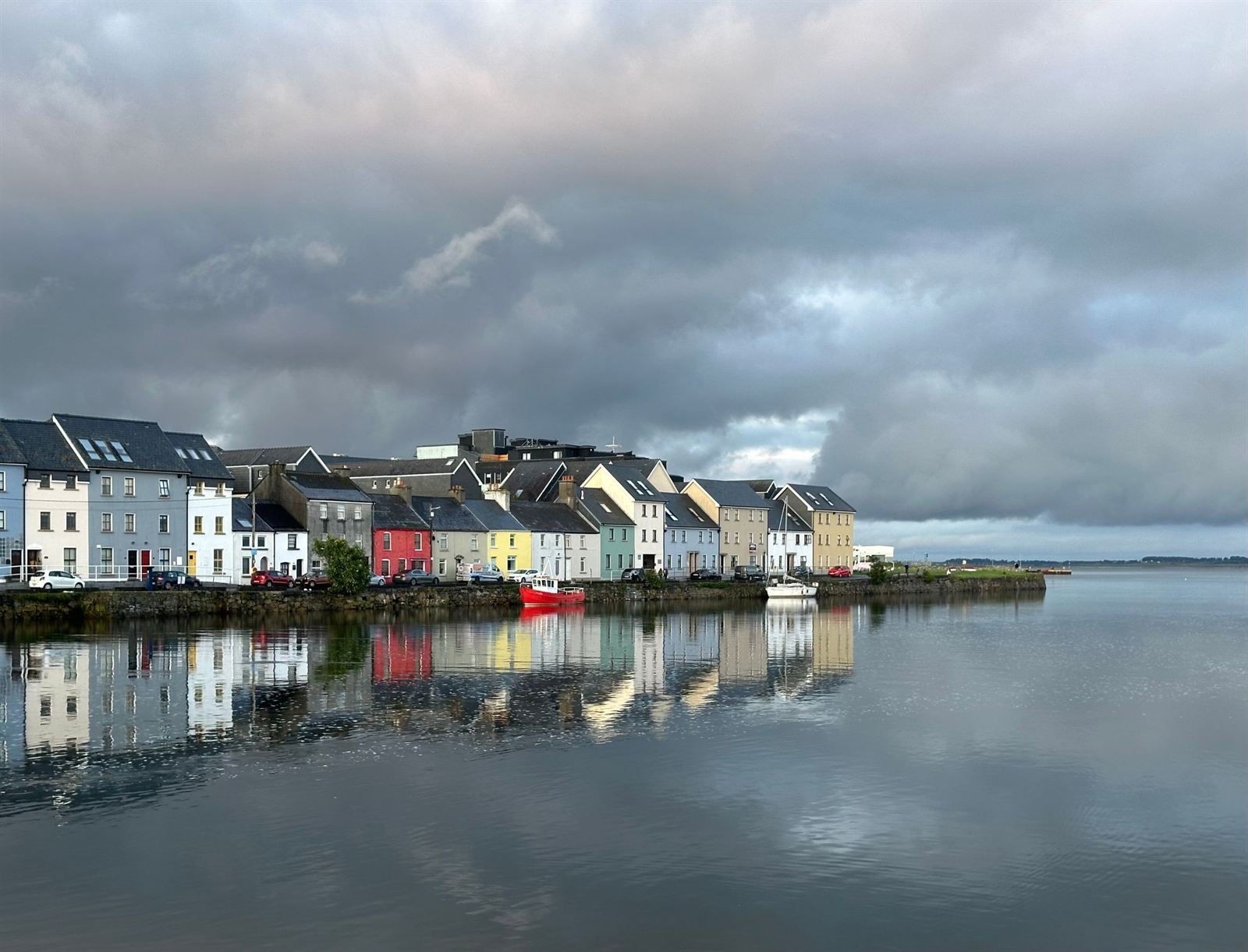 Colorful houses of the Long Walk in Galway reflected in calm water under a moody sky