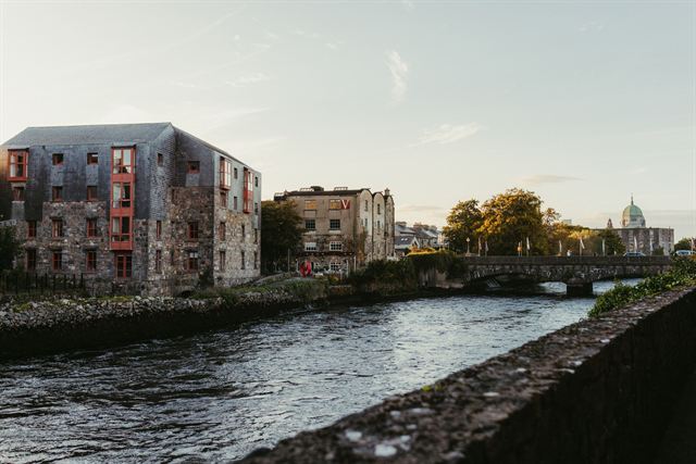 River Corrib in Galway city with stone buildings, a bridge and the cathedral dome at dusk