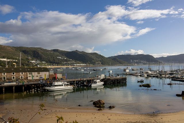 Knysna Lagoon waterfront with jetties, boats and forested hills under blue sky
