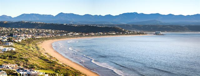 Aerial panorama of the long sandy curve of Plettenberg Bay with seaside homes and mountains