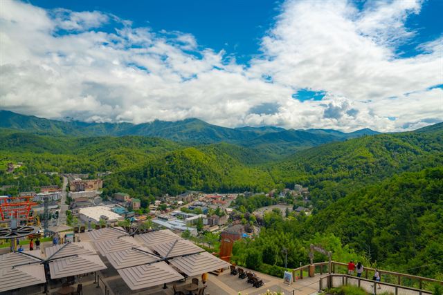Aerial view over Gatlinburg, Tennessee rooftops toward green ridges of the Great Smoky Mountains under puffy clouds