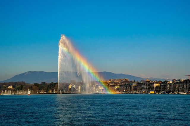 Jet d'Eau fountain in Lake Geneva with a rainbow in its spray and Geneva waterfront behind