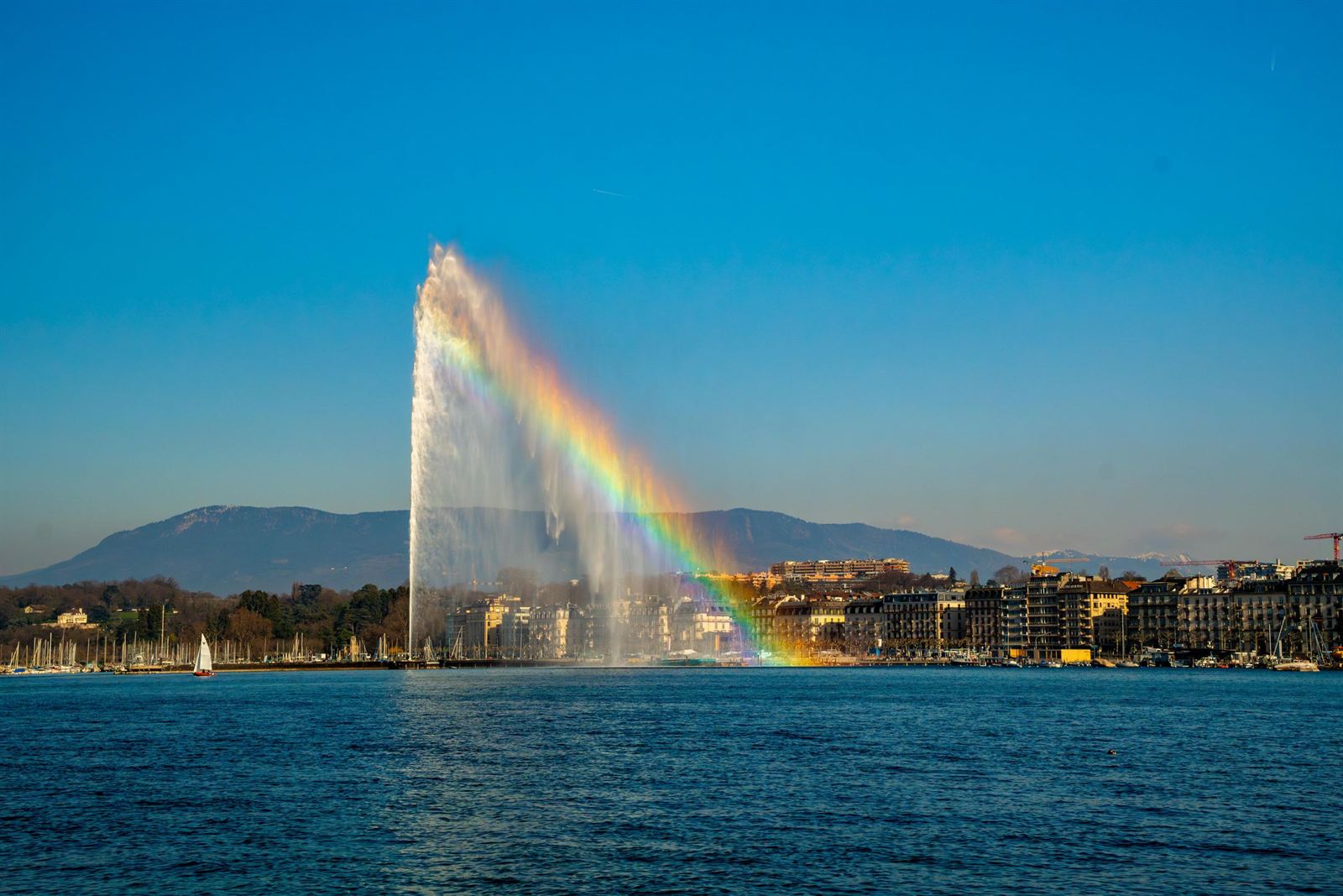 Jet d'Eau fountain in Lake Geneva with a rainbow in its spray and Geneva waterfront behind