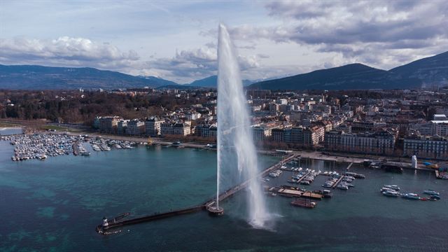 Elevated view of Geneva harbor, the Jet d'Eau fountain, marinas and city with mountains beyond