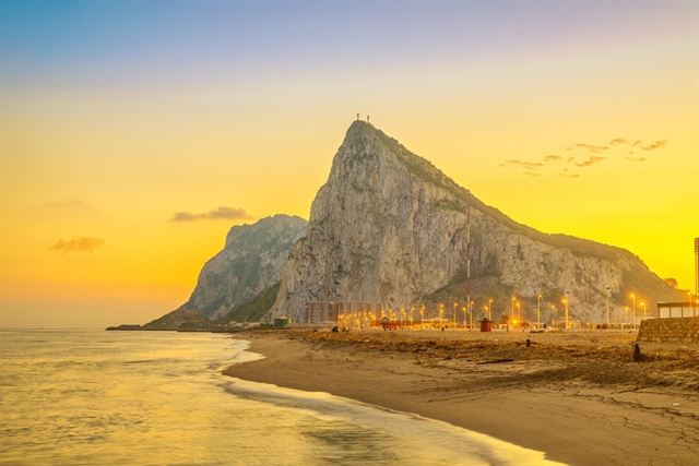 Rock of Gibraltar at sunset seen across a sandy beach with town lights at its base