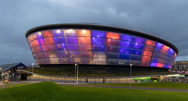 OVO Hydro arena in Glasgow lit in purple, pink and blue at dusk beside the River Clyde