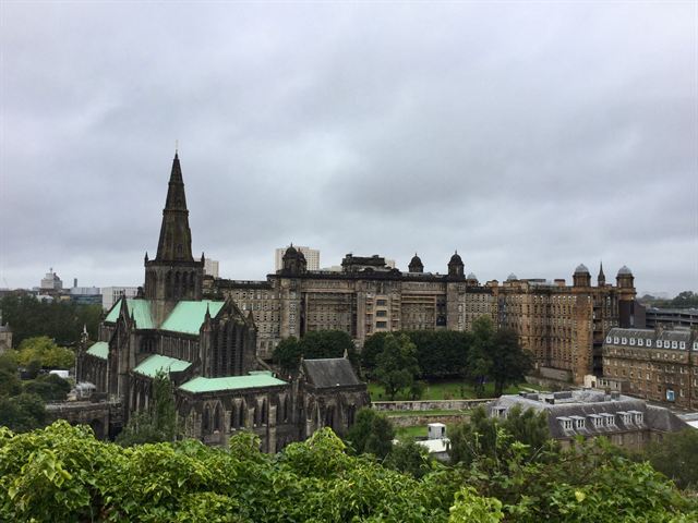 Glasgow Cathedral's spire and green copper roofs with the Royal Infirmary behind under grey sky