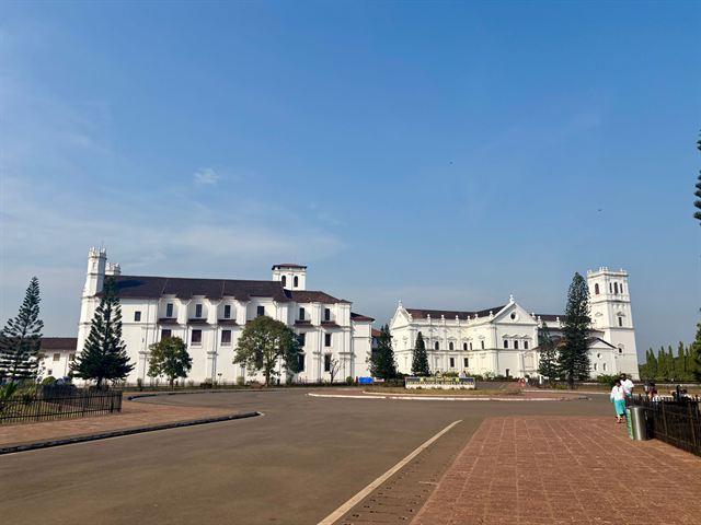 Whitewashed Se Cathedral and neighboring church facades across the plaza in Old Goa, India, under blue sky
