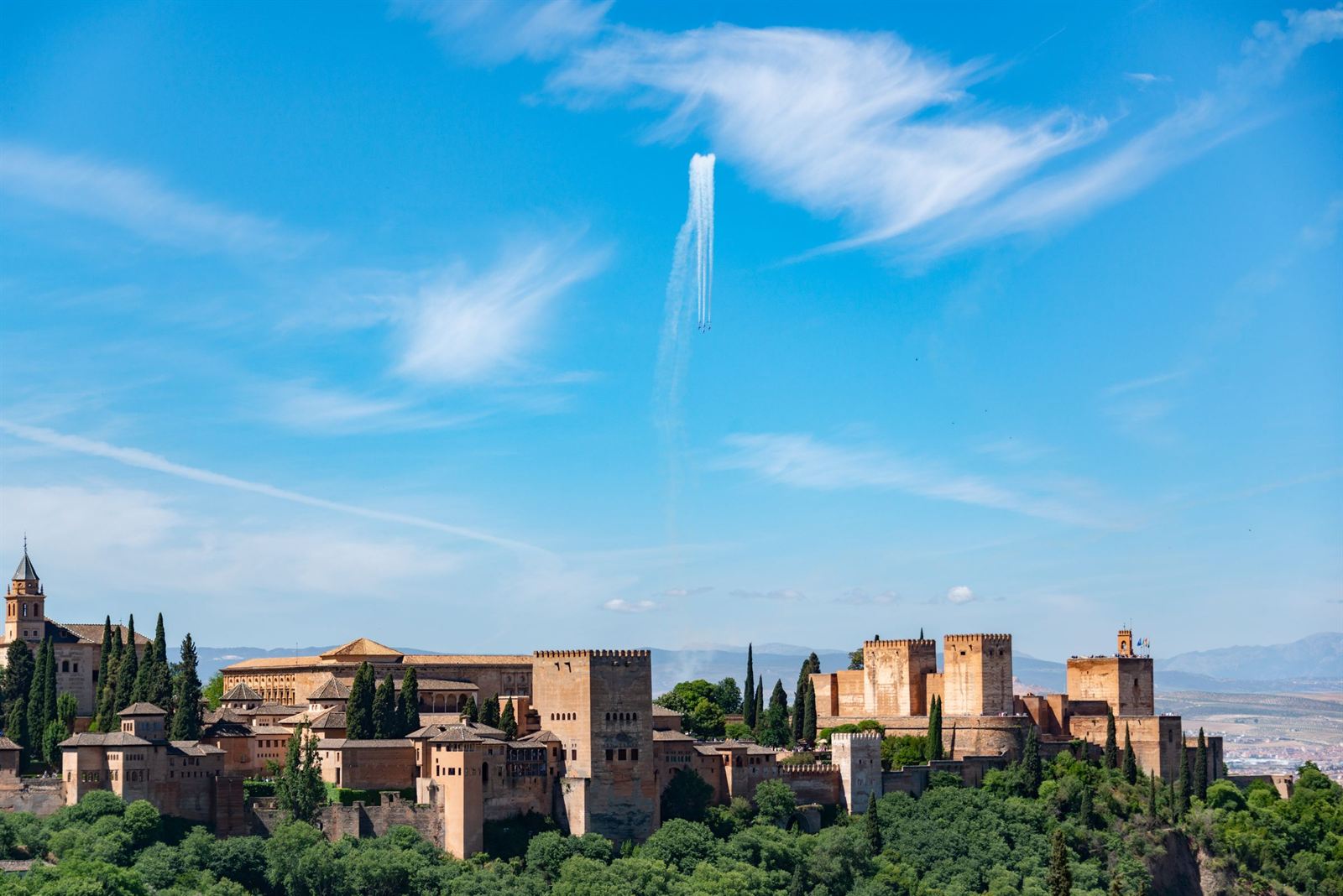The Alhambra palace and fortress walls in Granada above green woods under bright blue sky