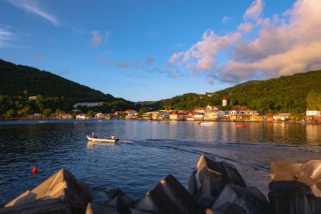Deshaies bay in Guadeloupe with a small boat, waterfront village and green hills at sunset