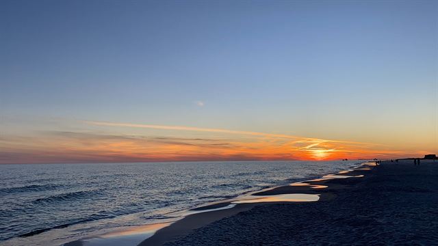 Sunset over the Gulf of Mexico at Gulf Shores, Alabama with gentle waves along a dark sandy beach