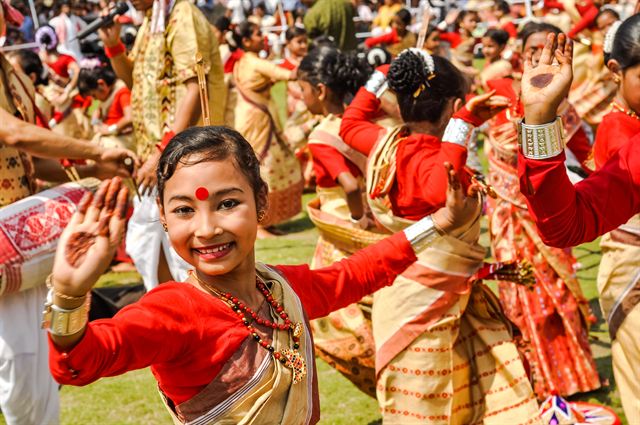 Smiling dancer in a red and gold sari performing the Bihu dance in Guwahati, Assam