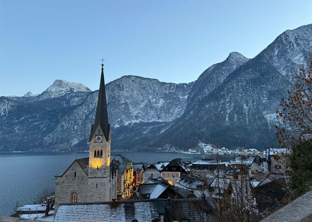 Hallstatt's church spire and village rooftops at dusk with snow-dusted Dachstein peaks behind