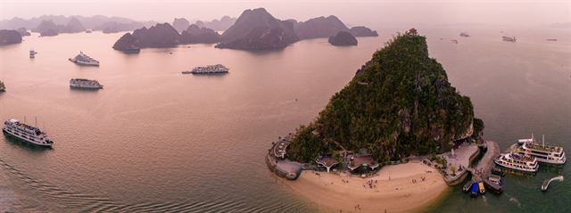 Tour boats anchored around Ti Top Island and limestone karst islets in Halong Bay at dusk