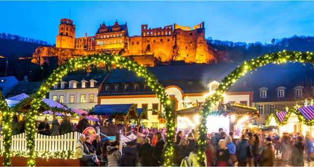 Heidelberg Christmas market stalls under lit arches with the floodlit castle ruins above at night