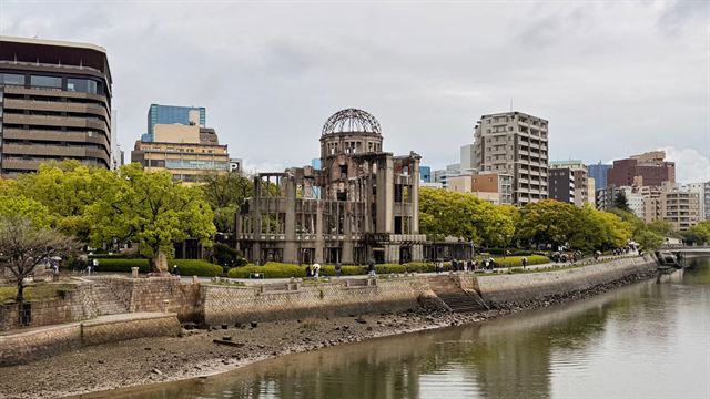 Atomic Bomb Dome beside the Motoyasu River in Hiroshima with trees and city buildings behind