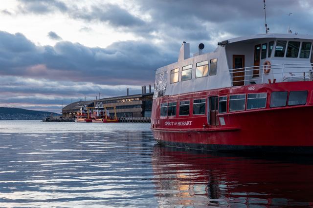 Red harbor ferry moored on calm water at the Hobart waterfront under a cloudy sky