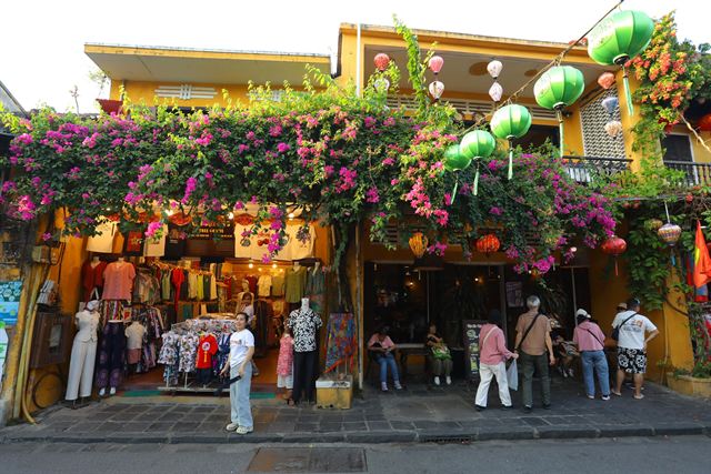 Yellow Hoi An shophouse draped in bougainvillea and green silk lanterns above a street shop