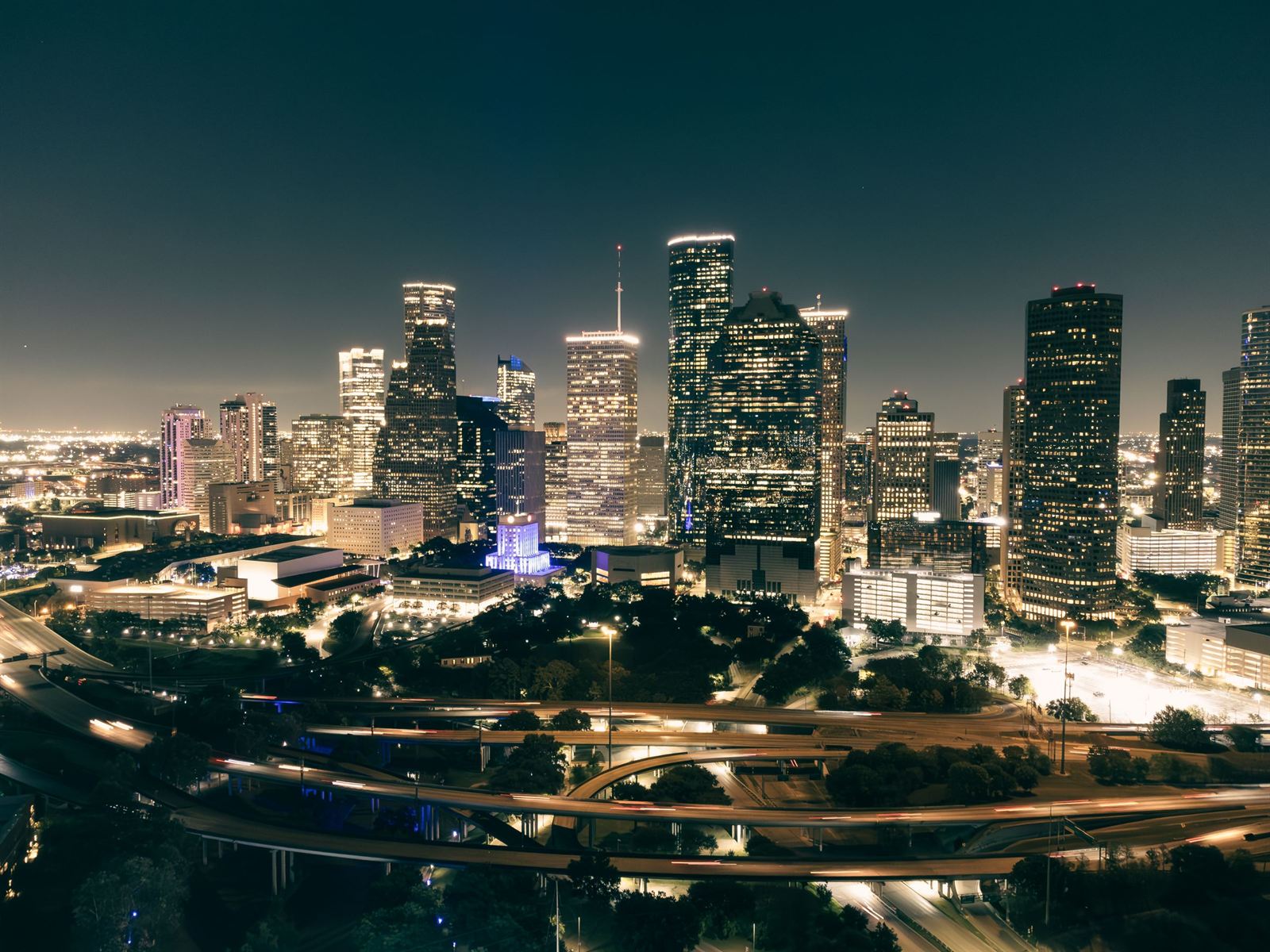 Aerial night view of the illuminated downtown Houston skyline above looping freeways