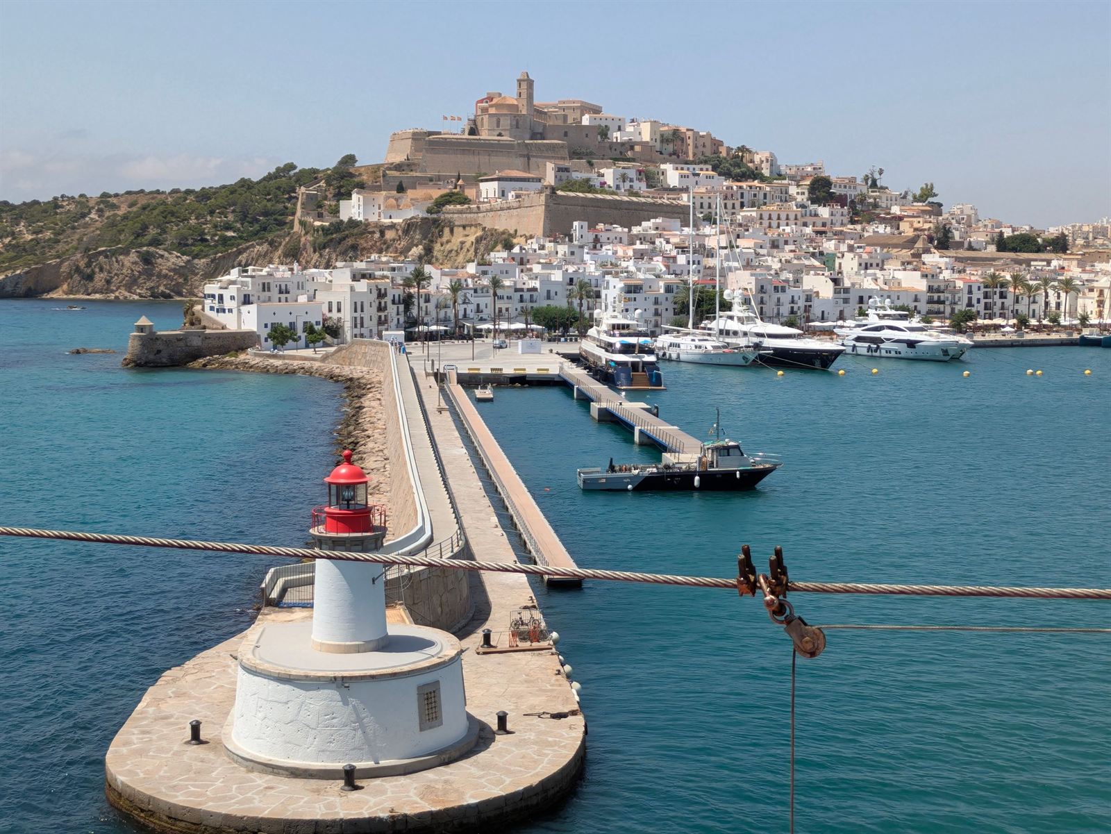 Ibiza Town harbor with red-and-white lighthouse on the breakwater and walled Dalt Vila on the hill