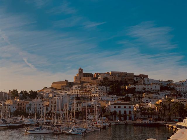 Dalt Vila old town and cathedral of Ibiza glowing at dusk above sailboats in the harbor