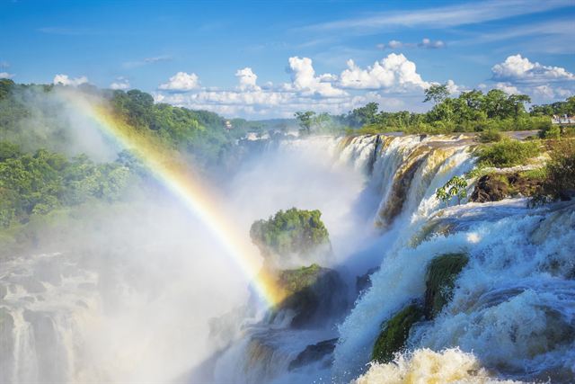 Rainbow in the spray of Iguazu Falls under blue sky