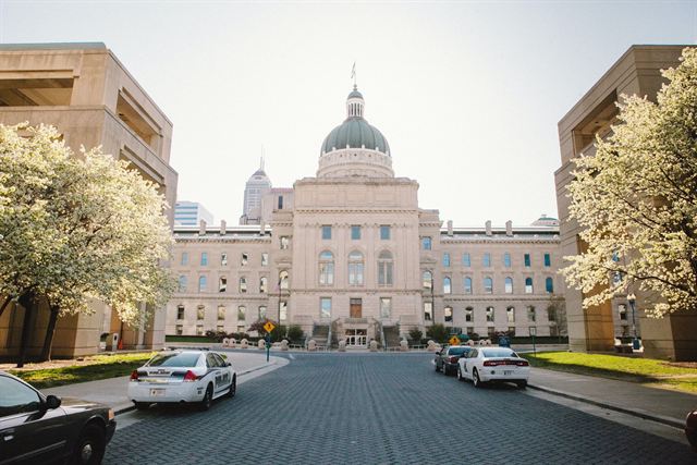Indiana Statehouse with its dome framed by blossoming trees along a brick drive in Indianapolis