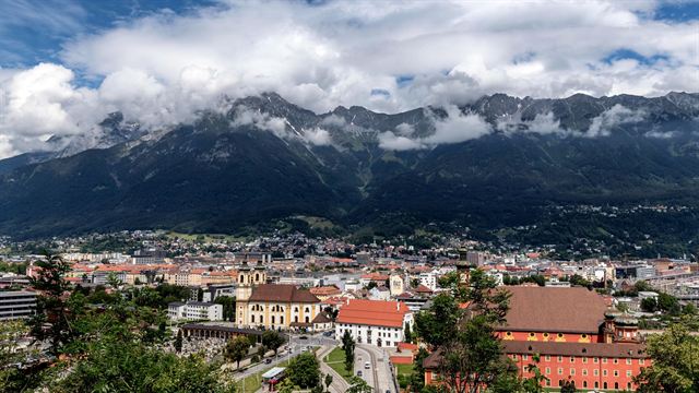 Panorama of Innsbruck's rooftops and churches below cloud-wrapped Alpine peaks