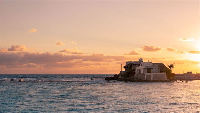 Seafront villa on rocks silhouetted against a golden sunset over the bay at Isla Mujeres, Mexico