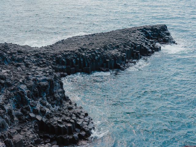 Hexagonal basalt columns of the Jusangjeolli cliffs meeting blue sea on Jeju Island, South Korea