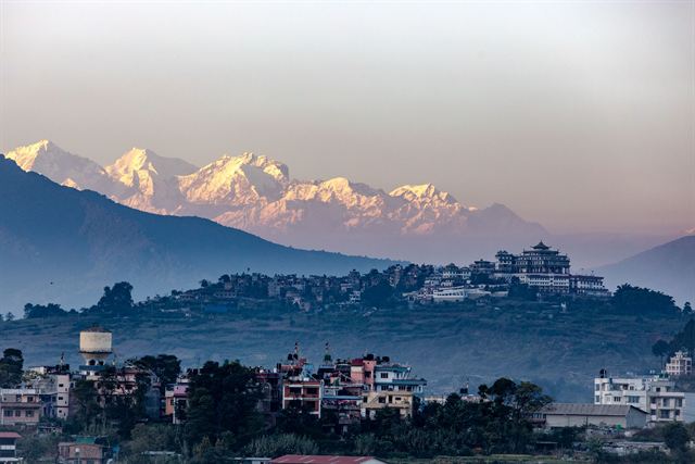 Kathmandu Valley at sunset with a hilltop monastery and snowy Himalayan peaks beyond