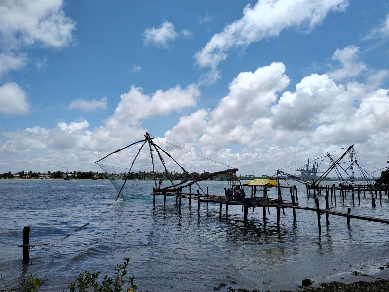 Chinese fishing nets on wooden platforms at Fort Kochi under blue sky and white clouds