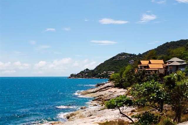 Rocky Koh Samui shoreline with deep blue sea and resort villas on a green hillside