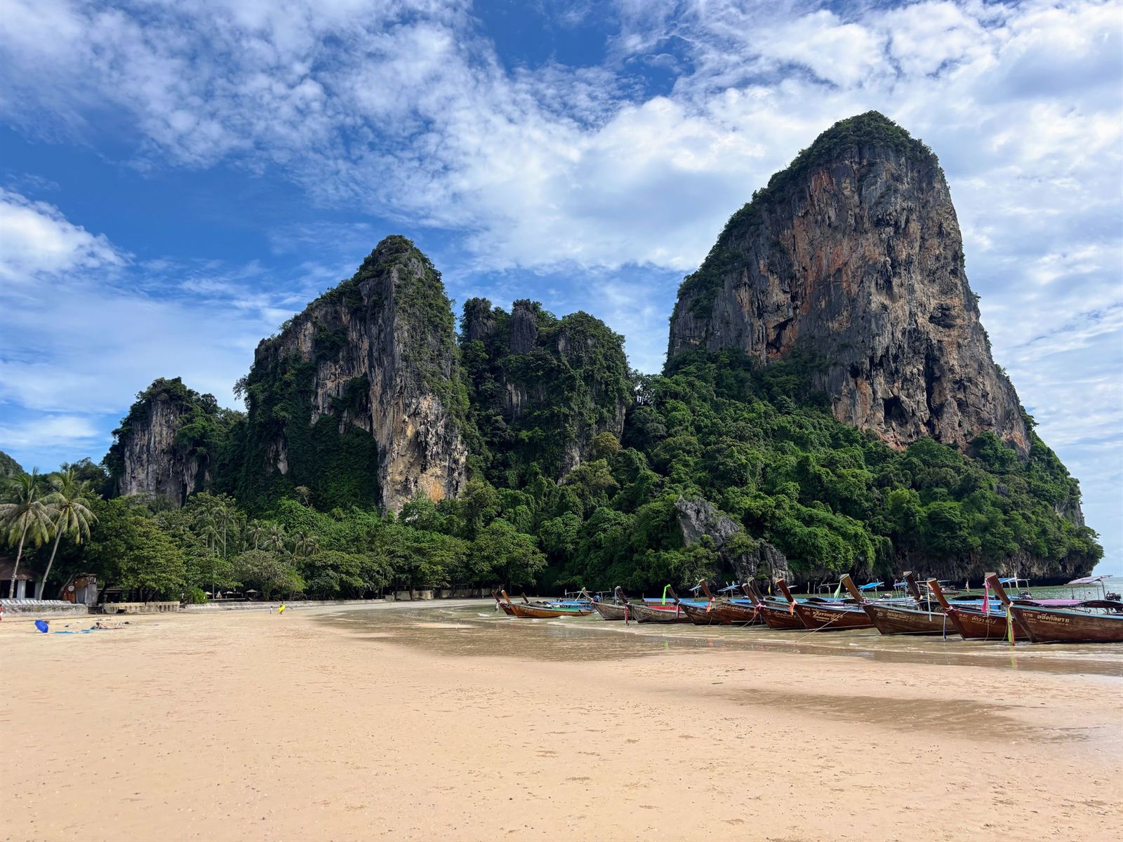 Towering limestone karst cliffs above the sandy beach and longtail boats at Railay Beach, Krabi