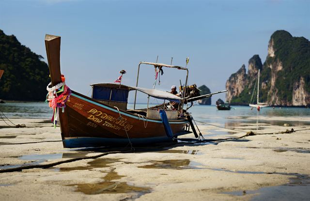 Decorated longtail boat beached at low tide in Krabi with jungle-covered limestone karsts behind