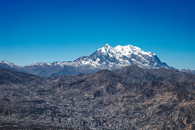 Sprawling La Paz city filling the valley below the snowy Illimani massif under deep blue sky