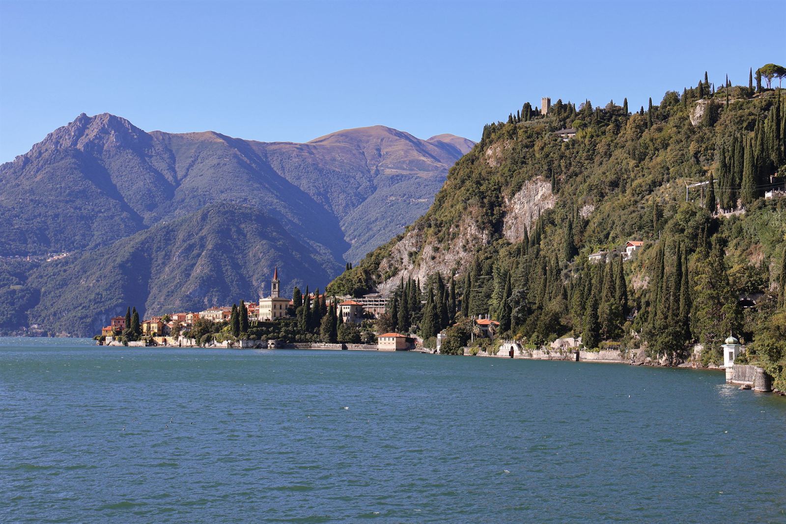 Lake Como shoreline at Varenna with lakeside villas beneath steep wooded slopes and purple mountains