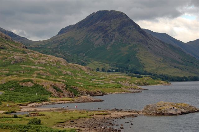Rocky green fell rising above a lake shore in the Lake District National Park under grey clouds