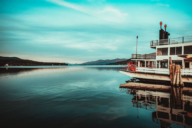 Lake George paddlewheel steamboat at its dock with calm water and mountains under a teal sky