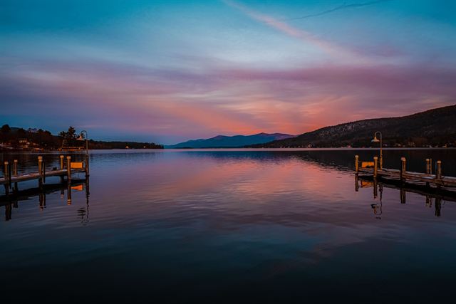 Sunset over calm Lake George, New York with wooden docks and silhouetted mountain ridges