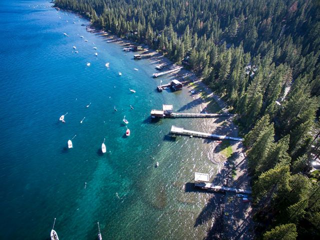Aerial view of piers, moored boats and turquoise shallows along Lake Tahoe's forested shoreline