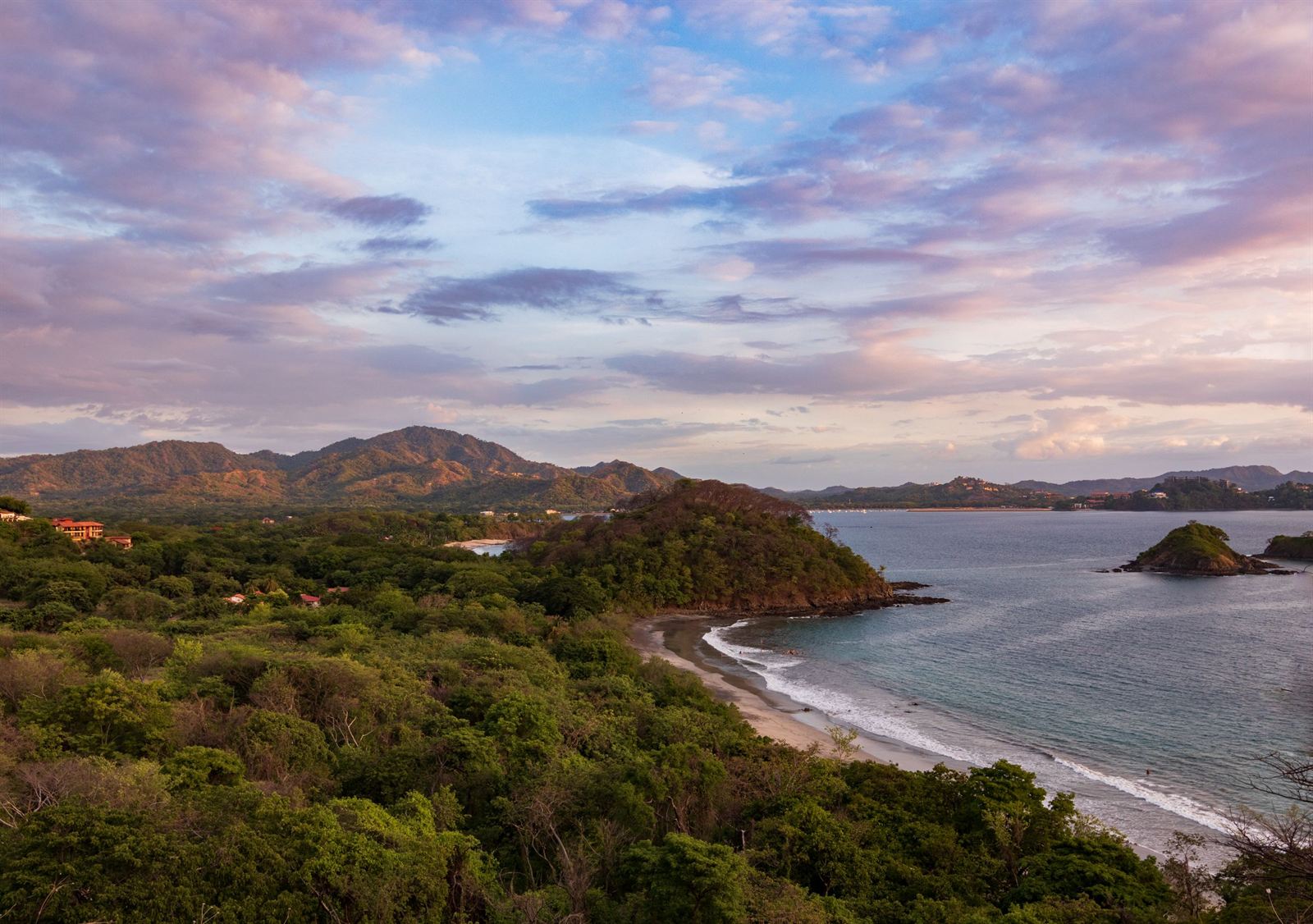 Forested Guanacaste coastline and sandy bay on the Papagayo Peninsula under a pink sunset sky