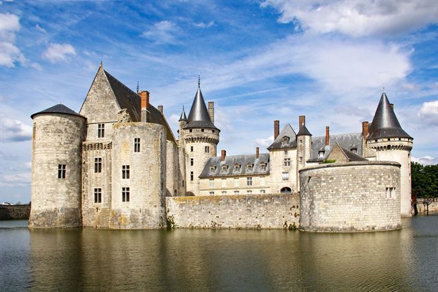 Chateau de Sully-sur-Loire with pointed turrets reflected in its moat under blue sky