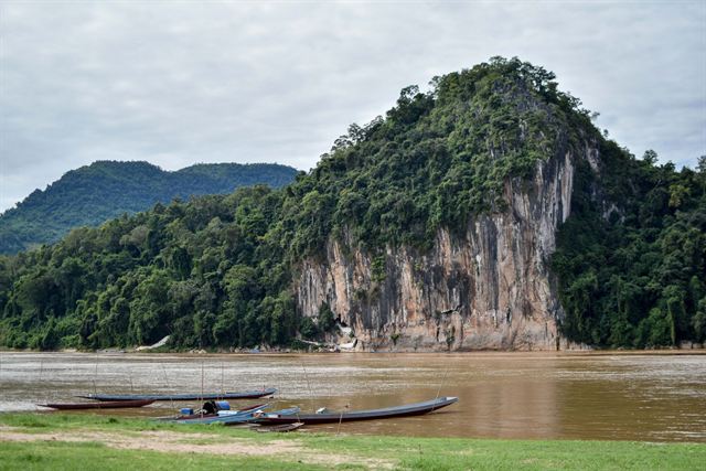 Longboats on the Nam Ou river below forested limestone cliffs near Luang Prabang, Laos