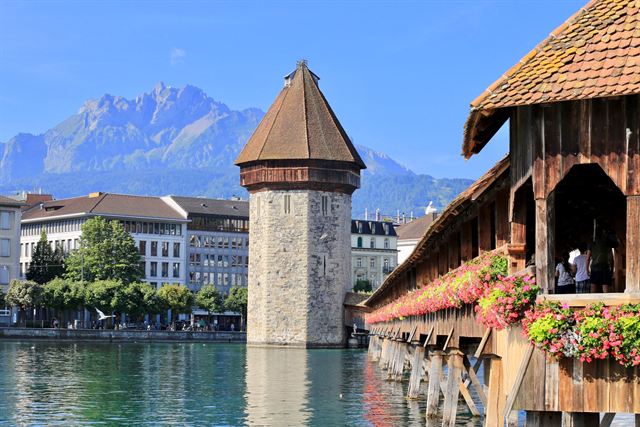 Water Tower and flower-decked Chapel Bridge in Lucerne with rugged Mount Pilatus behind
