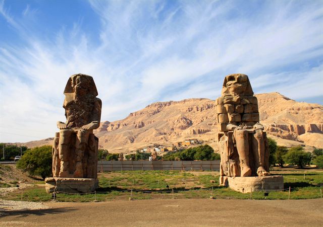 The twin seated Colossi of Memnon on the Luxor west bank below desert hills
